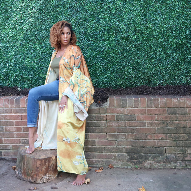 A woman models a flowing golden yellow Japanese kimono robe adorned with subtle olive branches, creating an elegant and nature-inspired design.