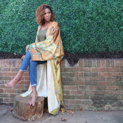 A woman poses in a flowing golden yellow Japanese kimono robe featuring olive branch details, offering an elegant, nature-inspired aesthetic.