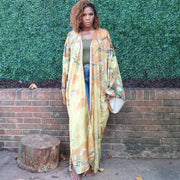 A woman showcases a golden yellow kimono robe with subtle olive branches, blending elegance with a serene, nature-inspired motif perfect for any occasion.