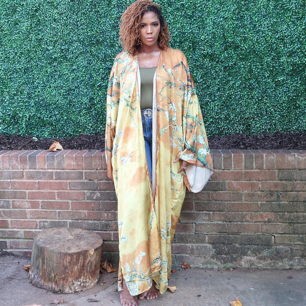 A woman showcases a golden yellow kimono robe with subtle olive branches, blending elegance with a serene, nature-inspired motif perfect for any occasion.