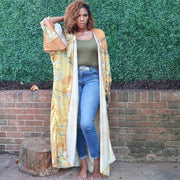 A model poses in a golden yellow kimono robe featuring delicate olive branch patterns, offering a graceful, flowing silhouette with earthy, natural accents.