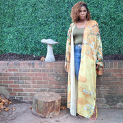 A woman models a golden yellow kimono robe adorned with olive branches, offering a stylish and flowing silhouette with a delicate, natural motif.