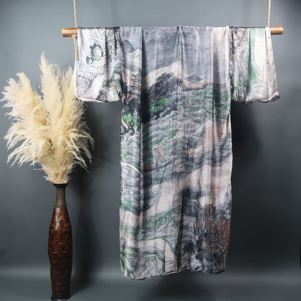 Grey mountains rivers and streams and a japanese hut decorate this kimono robe hung on display on a bamboo rod